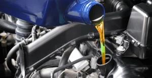 A close-up of golden synthetic motor oil being poured from a blue bottle into a car engine.